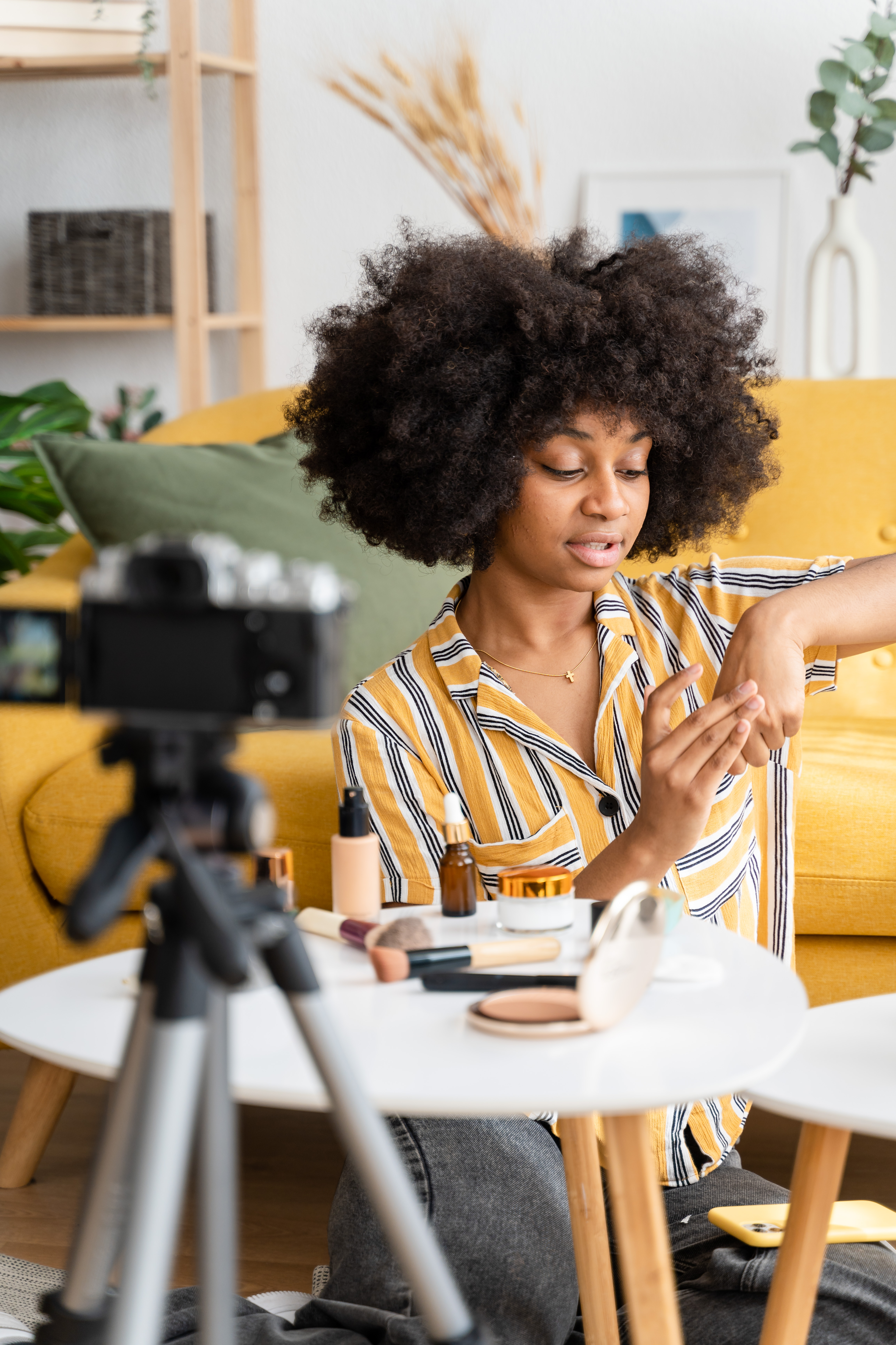 Positive African American female blogger with Afro hairstyle recording video on smartphone while sitting at home