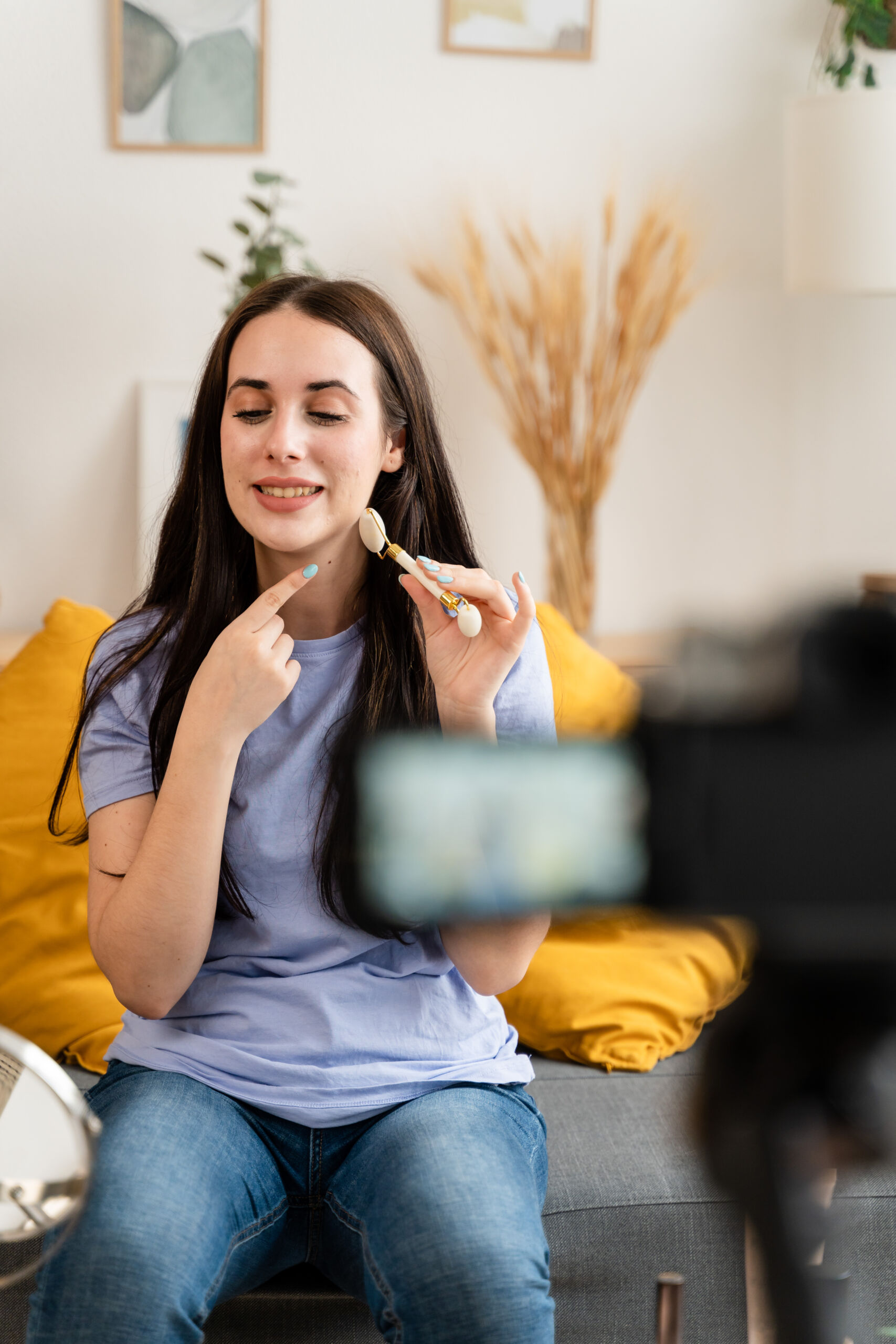 Streamer creating content for her social media about skin care, holding quartz roller in living room at home.